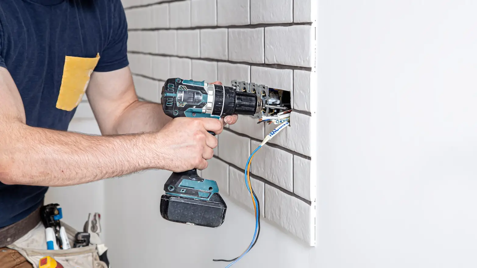 Electrician drilling wall near exposed electrical wires